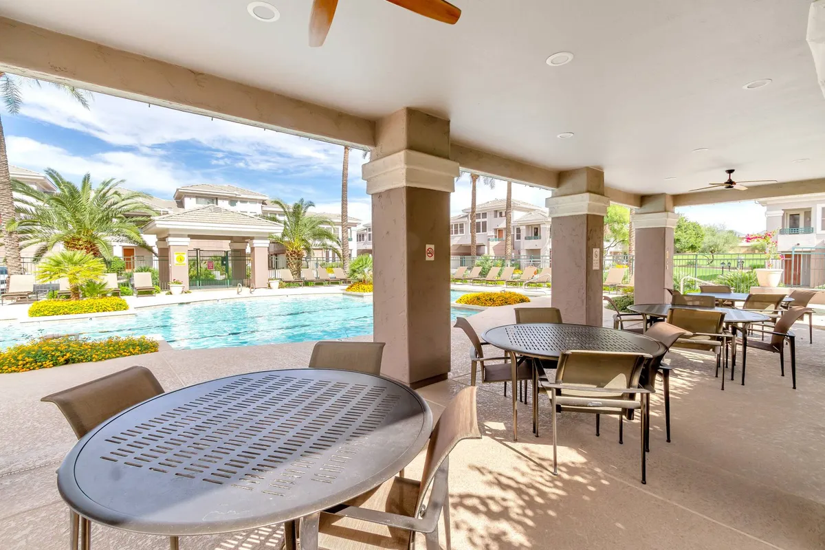 A vibrant exterior shot of the community's resort-style swimming pool surrounded by palm trees and landscaped gardens, with outdoor seating areas perfect for relaxation and social gatherings. The pool area is set aglow by the soft hues of sunset.