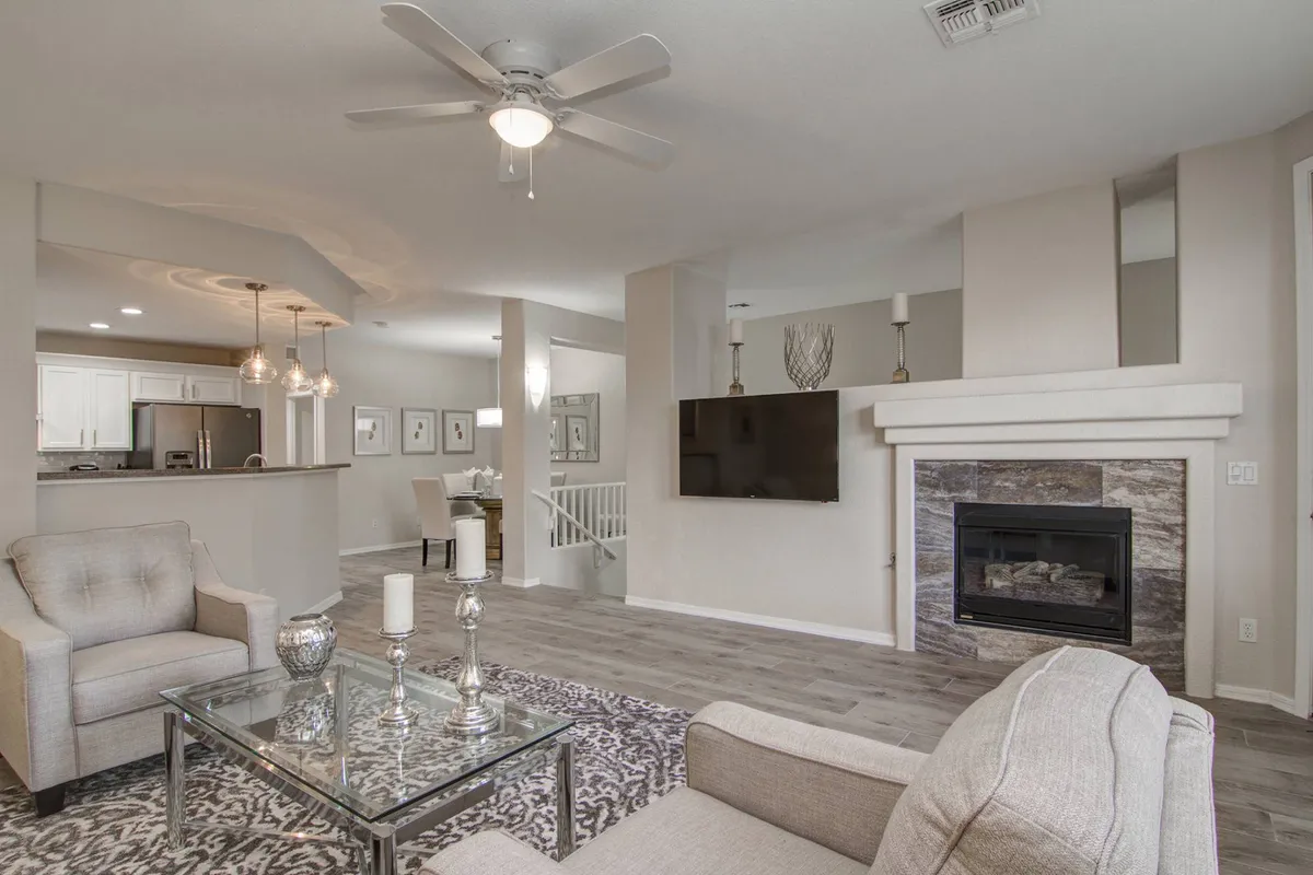 A welcoming living room scene with a glass coffee table, a custom gas fireplace, framed art on the walls, and a ceiling fan overhead. The space is arranged for socializing and comfort, perfect for cozy evenings or gatherings.