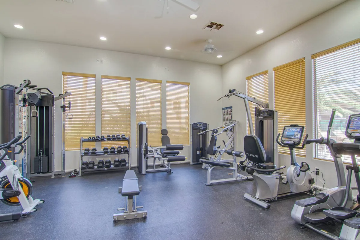 A well-equipped fitness center with various gym equipment, a dumbbell rack, and large windows that let in plenty of natural light. The space is designed for both individual workouts and communal fitness activities.