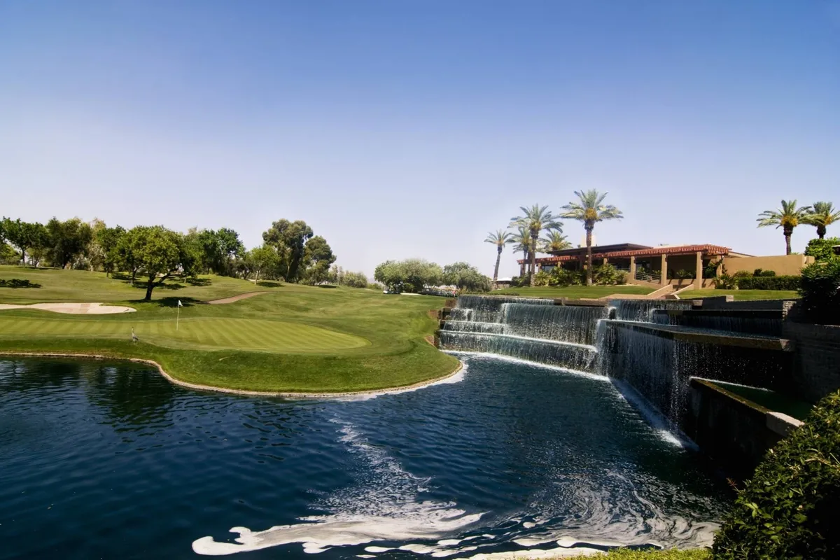 A sweeping exterior view of a lush golf course accented by a waterfall, swimming pool, and palm trees. The scene exudes a sense of relaxation, outdoor recreation, and Scottsdale's signature resort lifestyle.