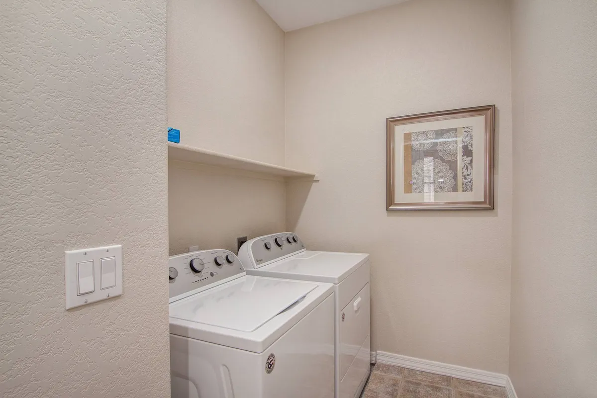 A well-organized laundry space featuring modern washing machines, framed artwork, and a convenient shelf above the units for storage. The setup feels tidy, practical, and ready for extended stays.