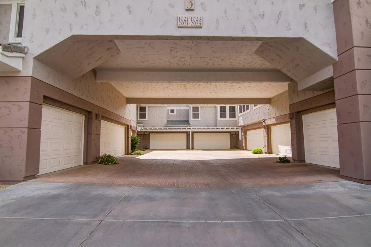 A practical and organized garage area with multiple garage doors and a paved driveway under an overhead structure. The environment feels safe, welcoming, and conducive to community living.