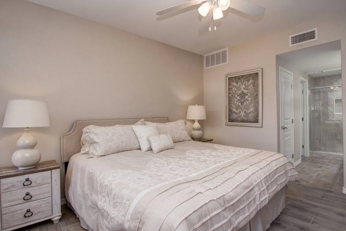 A tranquil master bedroom featuring a king-sized bed adorned with premium linens, a nightstand with a lamp for evening reading, and tasteful decorative artwork above the bed. Soft natural light filters in, creating a cozy and restful atmosphere, ideal for relaxation after a day in the sun.