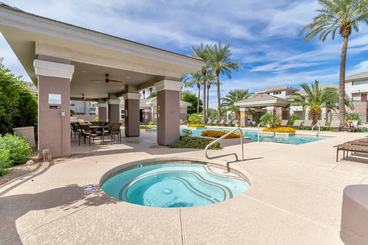 This exterior image showcases a resort-style swimming pool and hot tub surrounded by comfortable outdoor seating and lush palm trees. The setting is tranquil and inviting, ideal for relaxing poolside, sunbathing, or enjoying a soak in the hot tub beneath the open sky.