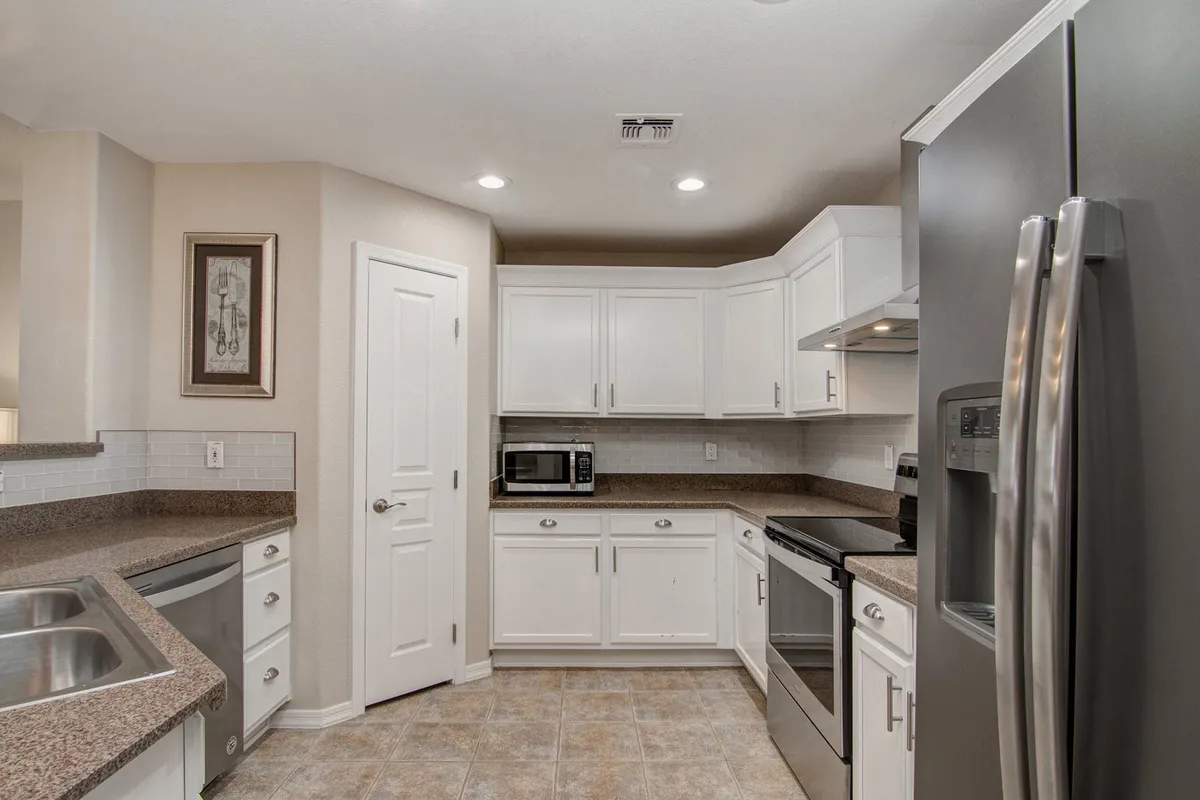 A bright, modern kitchen with white cabinetry, granite countertops, and stainless steel appliances. Artful decor adds warmth, making the area feel both functional and homey for preparing family meals.