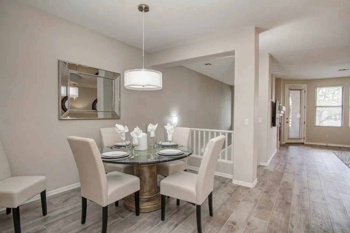 An elegant dining area featuring a circular dining table beneath a stylish chandelier, with a mirror reflecting the space. The setting is inviting, perfect for family dinners and creating lasting memories.