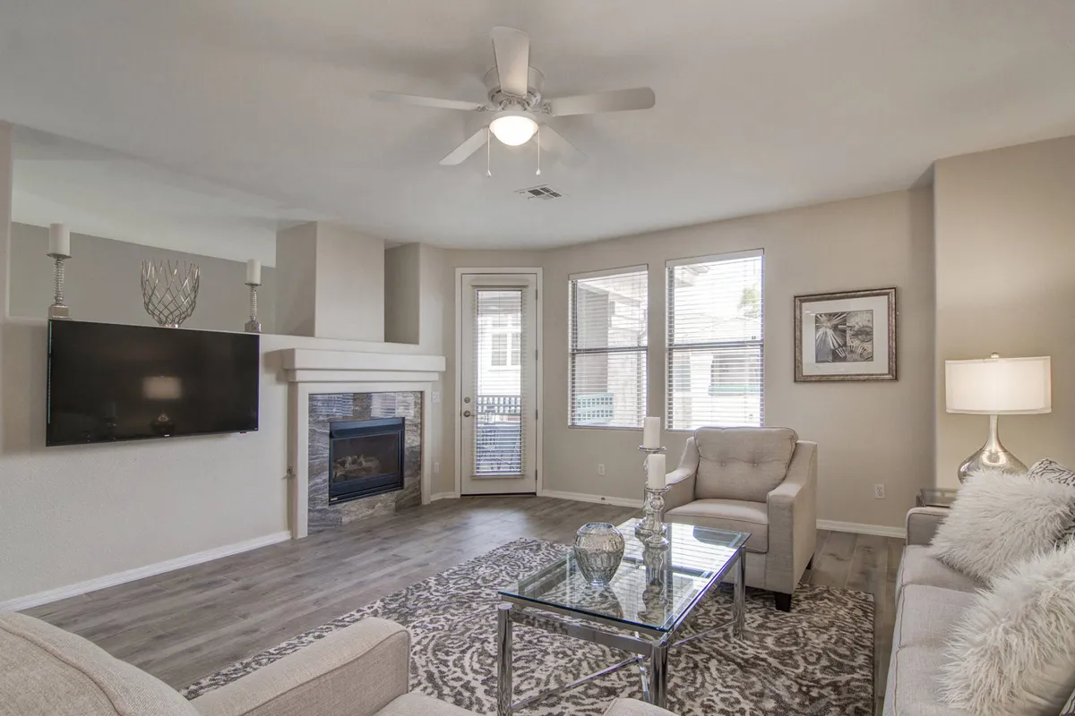The image showcases a stylish, professionally decorated living room with a cozy fireplace as the centerpiece, a comfortable sofa and coffee table arranged for conversation, a flat-screen TV for movie nights, and large windows that let in natural Arizona light.